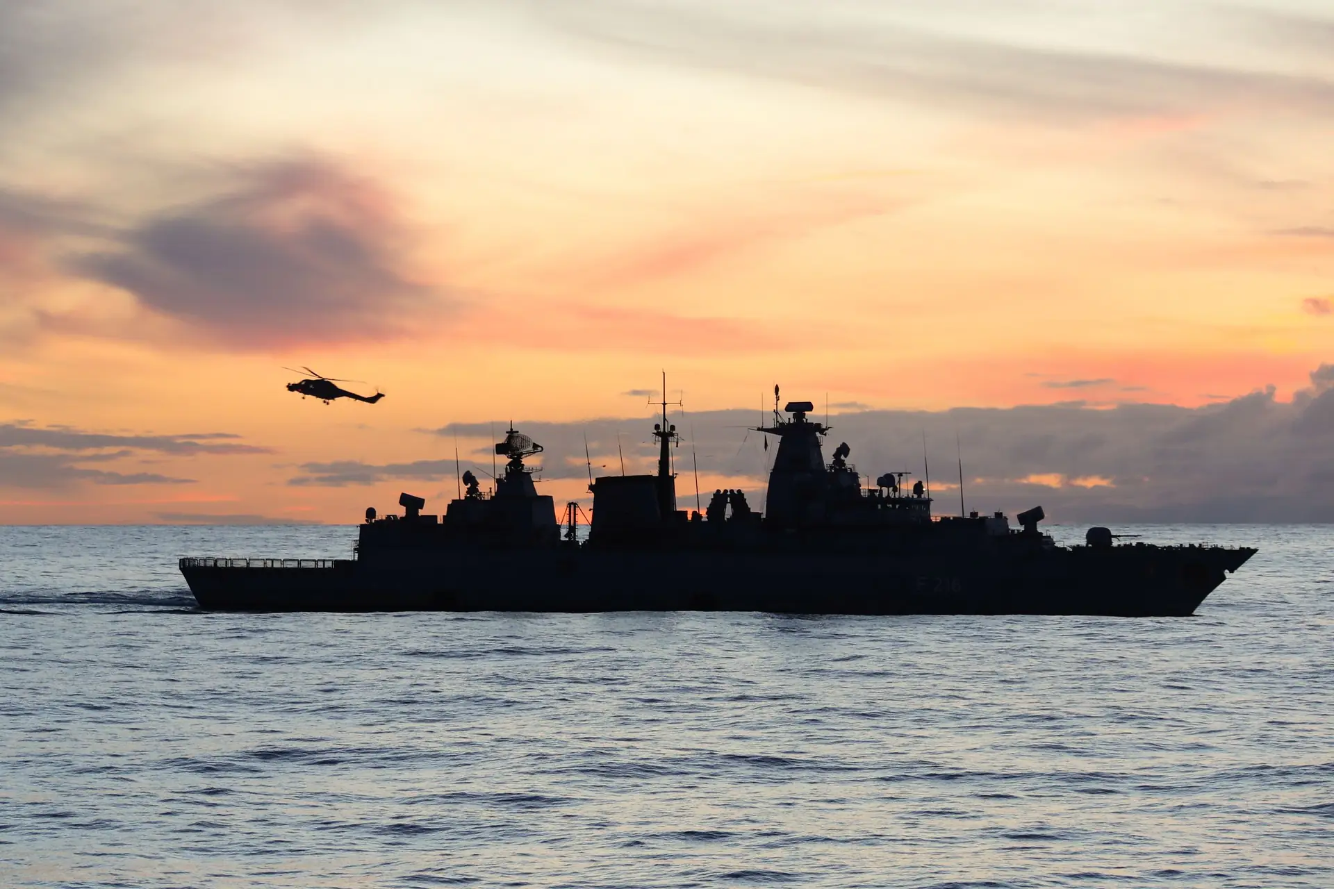 Naval frigate and helicopter silhouetted at sunset